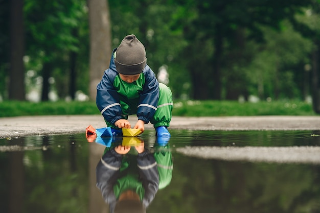 Niño gracioso en botas de lluvia jugando en un parque de lluvia