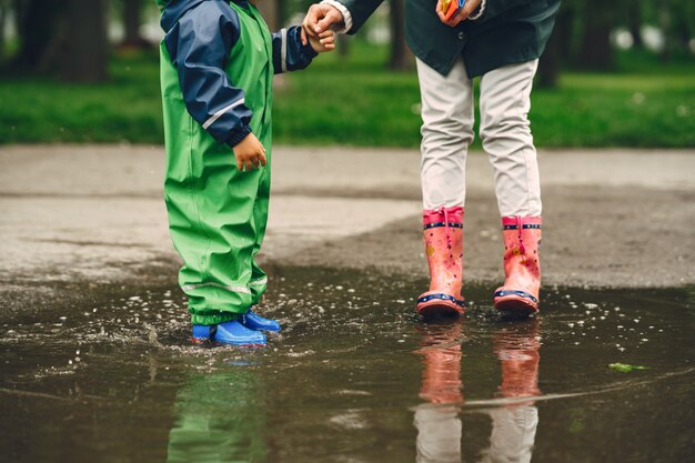 Niño gracioso en botas de lluvia jugando en un parque de lluvia