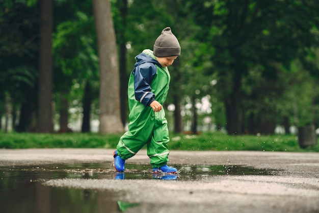 Niño gracioso en botas de lluvia jugando en un parque de lluvia