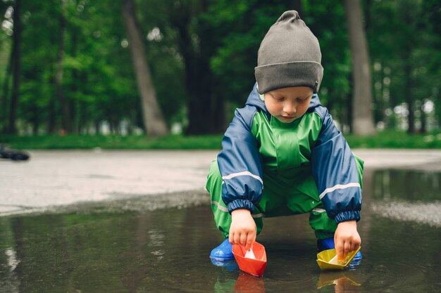Niño gracioso en botas de lluvia jugando en un parque de lluvia