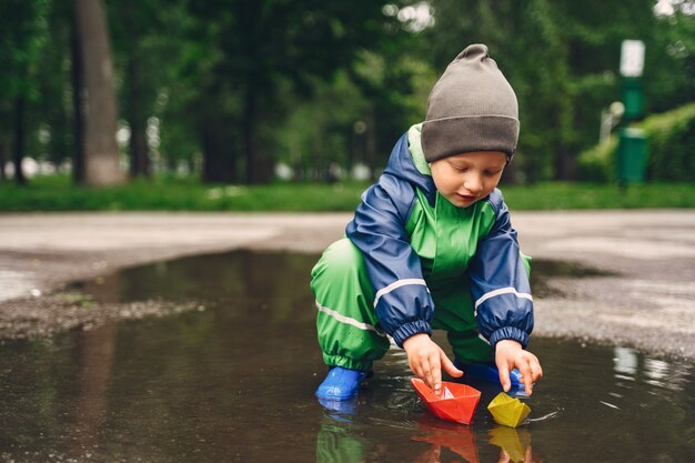 Niño gracioso en botas de lluvia jugando en un parque de lluvia