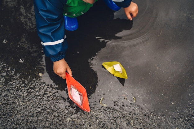 Niño gracioso en botas de lluvia jugando en un parque de lluvia