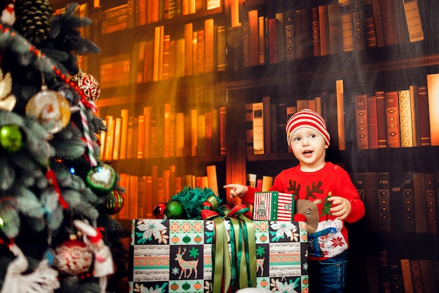 Niño gracioso juega con cajas presentes antes de un árbol de Navidad