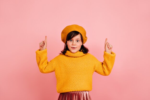 Niño gracioso. Niña francesa posando con las manos en la pared rosa.