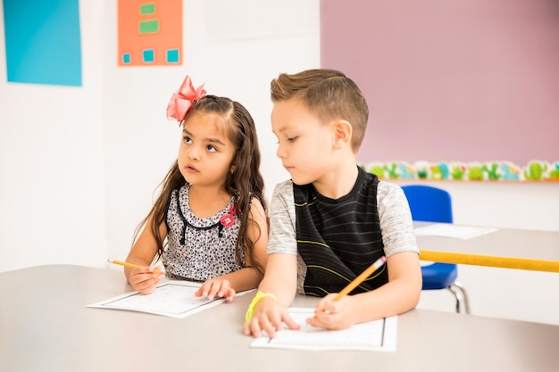 Niño guapo tratando de hacer trampa en una tarea de matemáticas en un aula de preescolar