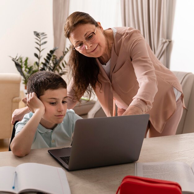 Niño haciendo los deberes con su abuela en la computadora portátil