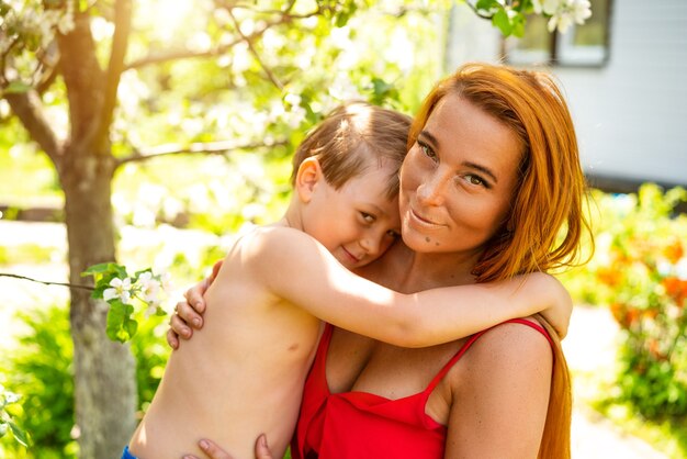 Un niño en un jardín floreciente abraza a una joven madre, el concepto de relaciones familiares. Día soleado de verano