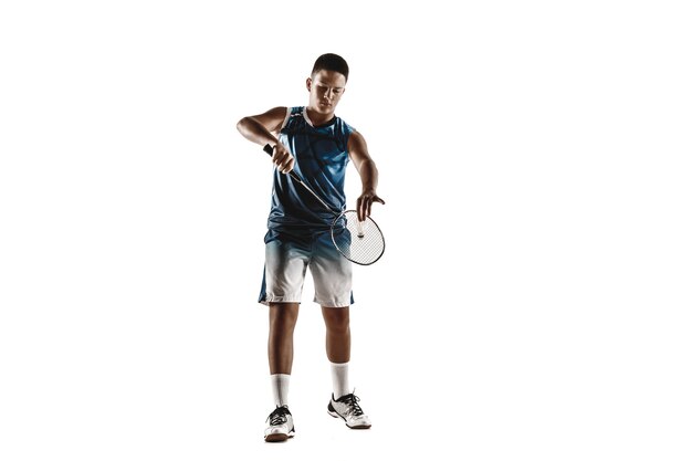 Niño jugando al bádminton aislado sobre fondo blanco de estudio. Modelo masculino joven en ropa deportiva y zapatillas con la raqueta en acción, movimiento en el juego. Concepto de deporte, movimiento, estilo de vida saludable.