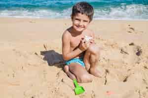 Foto gratuita niño jugando con concha en la playa