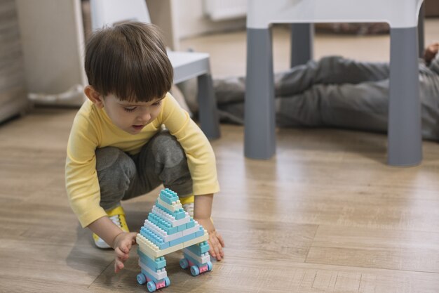 Niño jugando con juguete y padre piernas borrosas