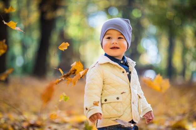 Niño jugando y lanzando hojas en el parque otoño