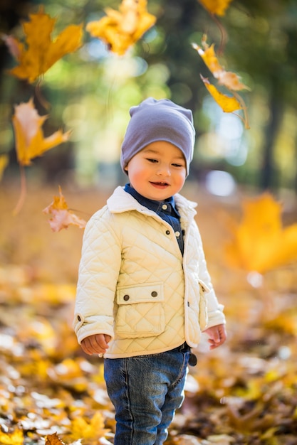 Niño jugando y lanzando hojas en el parque otoño