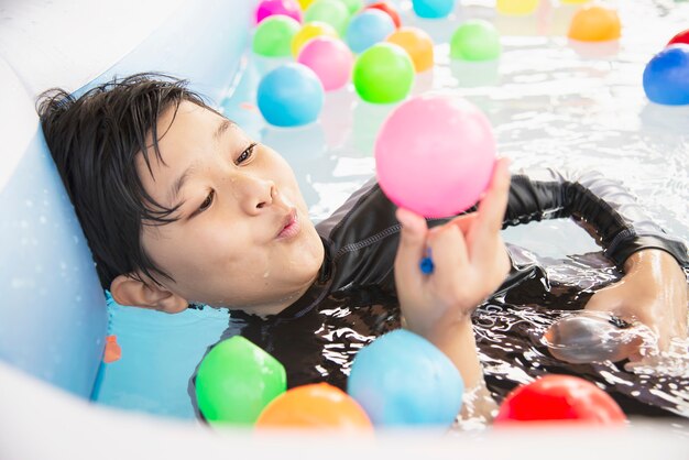 Niño jugando con pelota colorida en juguete de piscina pequeña