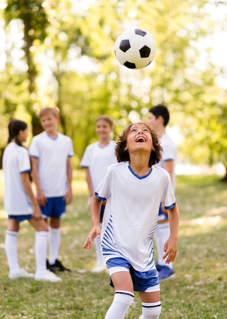 Niño jugando con una pelota de fútbol afuera junto a otros niños