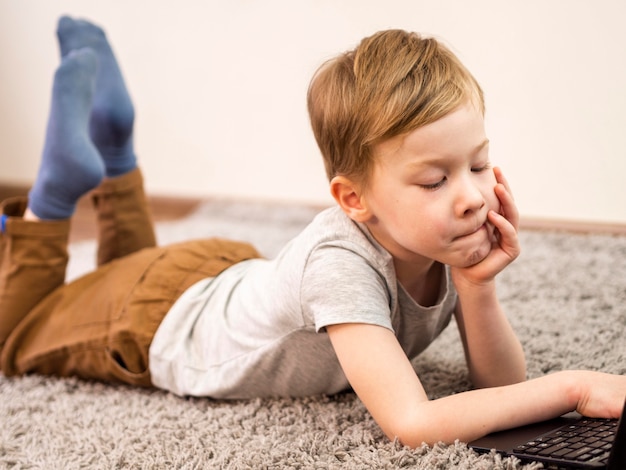 Foto gratuita niño jugando en su computadora portátil en el piso