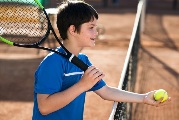 Niño de lado mostrando la pelota de tenis.