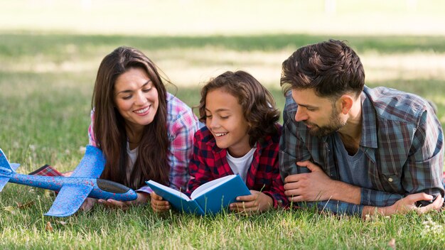 Niño leyendo en el parque con sus padres.