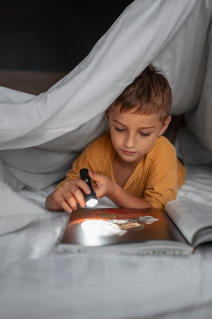 Niño leyendo revista con linterna tiro medio