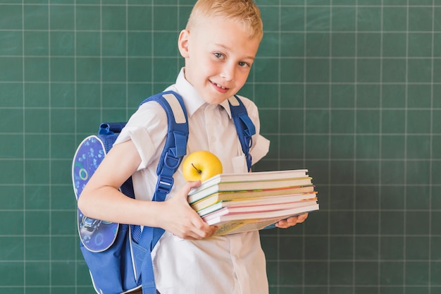 Foto gratuita niño con libros de texto y mochila cerca de la pizarra