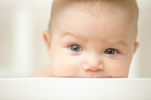 Niño lindo chupar una tabla de madera de la cuna blanca