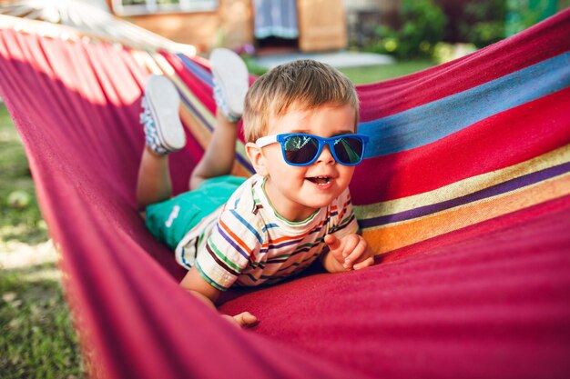 Niño lindo descansando en una hamaca brillante y divirtiéndose. en sus gafas de sol.