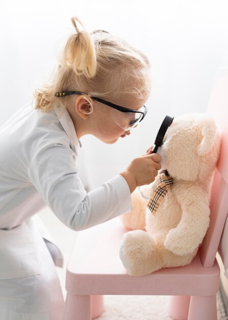 Niño lindo con gafas de seguridad sosteniendo lupa frente a oso de peluche