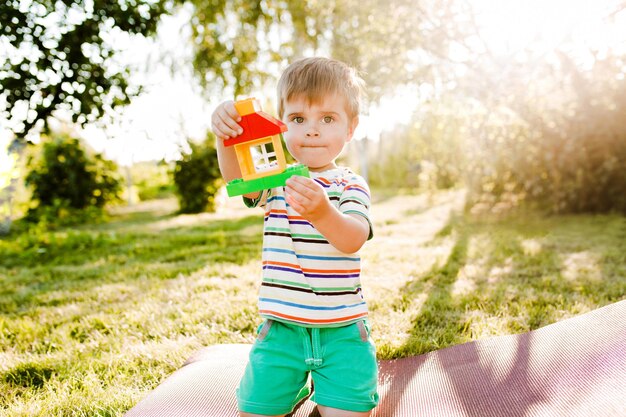 Niño lindo que sostiene una casa de juguete en el jardín y parece pensativo.