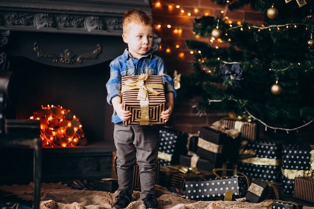 Niño lindo con regalo de navidad por árbol de Navidad