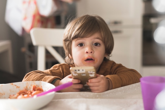 Niño lindo con teléfono en la mesa