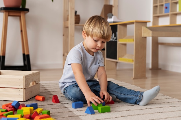 Niño lindo de tiro completo jugando en el piso con juguetes