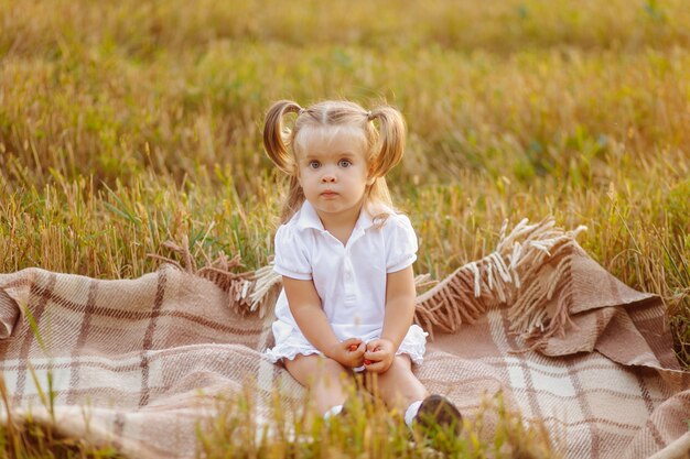 Niño lindo en vestido blanco posando en campo verde y