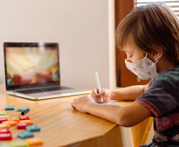 Niño con máscara médica y asistiendo a la escuela virtual