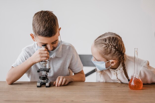 Niño con máscara médica mirando a través de un microscopio