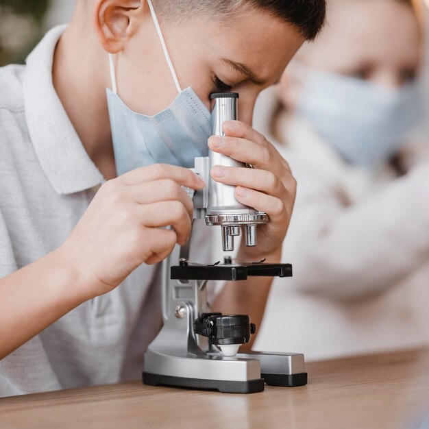 Niño con máscara médica mirando a través de un primer plano de microscopio