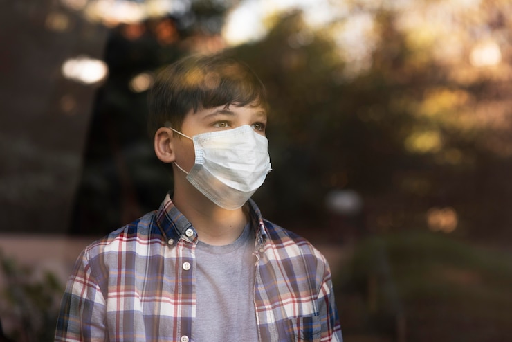 Foto gratuito niño con mascarilla mirando afuera a través de las ventanas