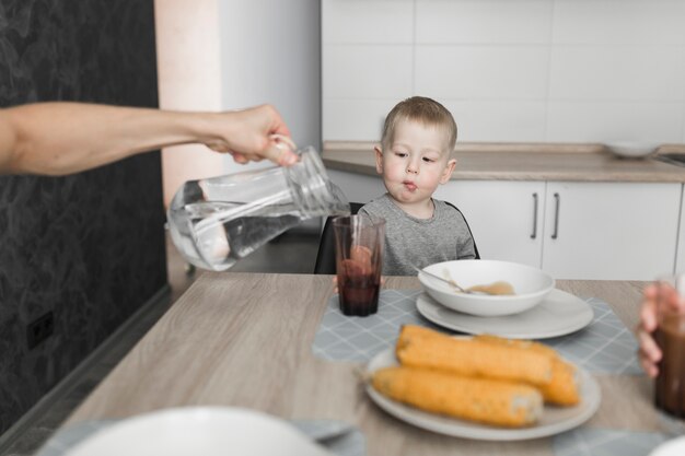 Un niño mirando a una persona vertiendo agua en el vaso en el desayuno