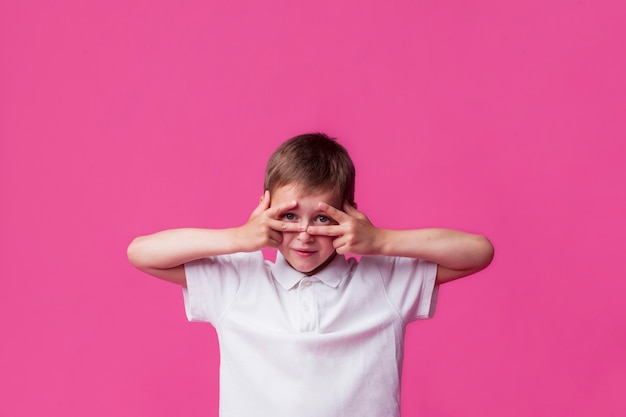 Foto gratuita niño mirando a través de v firmar sobre fondo rosa