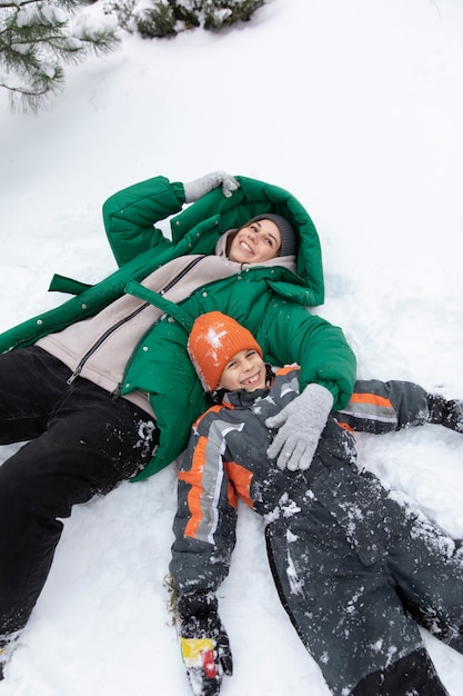 Niño y mujer de tiro medio tendidos en la nieve