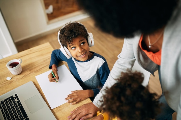 Niño negro feliz con auriculares hablando con su madre mientras aprende en casa