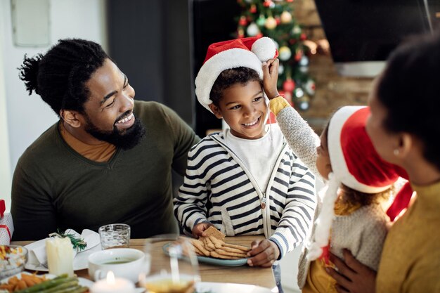 Niño negro feliz comiendo galletas y divirtiéndose con su familia en Navidad