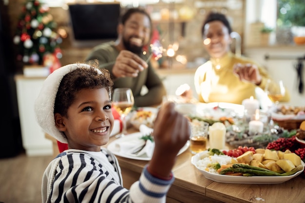 Niño negro feliz divirtiéndose con bengala mientras celebra la Navidad con su familia en casa