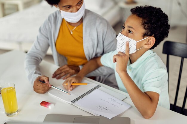 Niño negro pensando mientras aprende matemáticas con su madre en casa debido a la pandemia del coronavirus