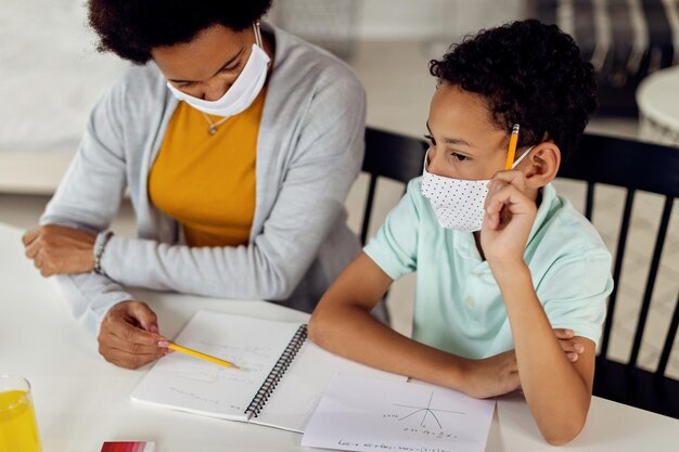 Niño negro pensativo educando en casa con su madre debido a la epidemia de coronavirus