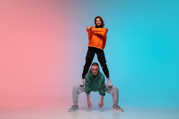 Niño y niña bailando hip-hop en ropa elegante sobre fondo degradado en el salón de baile en luz de neón.