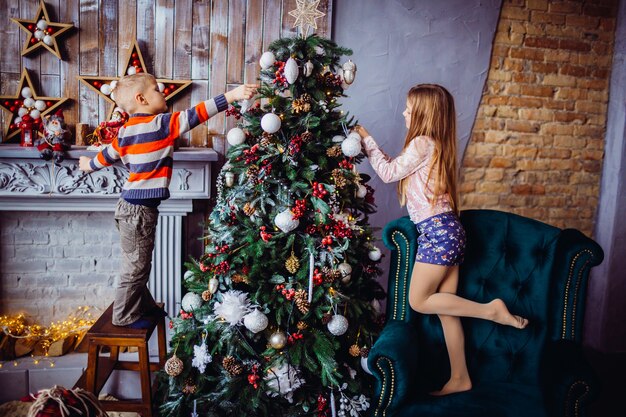 El niño y la niña bonita decorar un árbol de Navidad