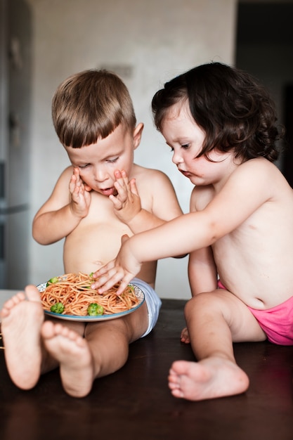 Foto gratuita niño y niña curiosos comiendo pasta