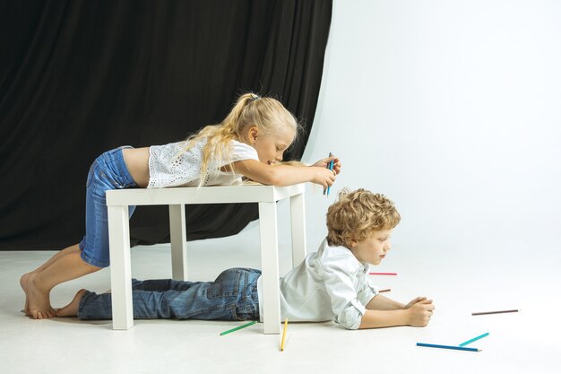 Niño y niña preparándose para la escuela después de un largo receso de verano. De vuelta a la escuela. Pequeños modelos caucásicos jugando juntos en el espacio