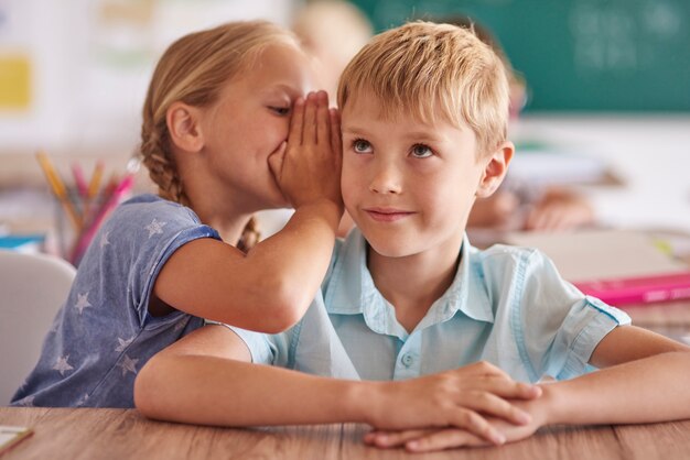 Niño y niña susurrando en el aula