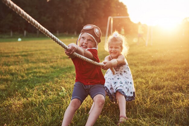 Niño y niña tirando de una cuerda y jugando tira y afloja en el parque