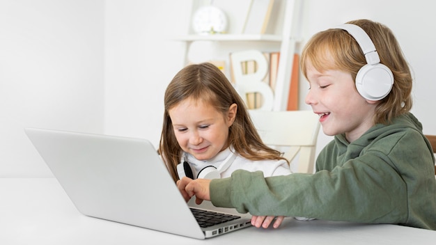 Niño y niña usando laptop con auriculares